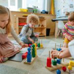 Preschool students sorting wooden geometric shapes sittings on the floor