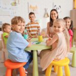 Little children with nursery teacher drawing at table in kindergarten