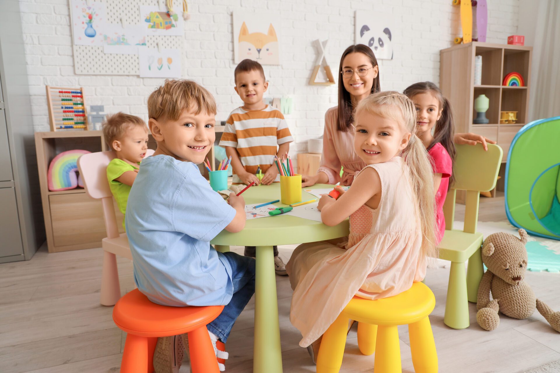 Little children with nursery teacher drawing at table in kindergarten